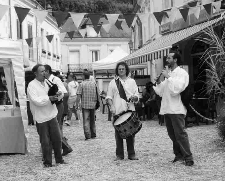 trio bombarde-biniou-tambour dans les rues couvertes de pailles et bordées de vieux batiments d'un marché à l'ancienne